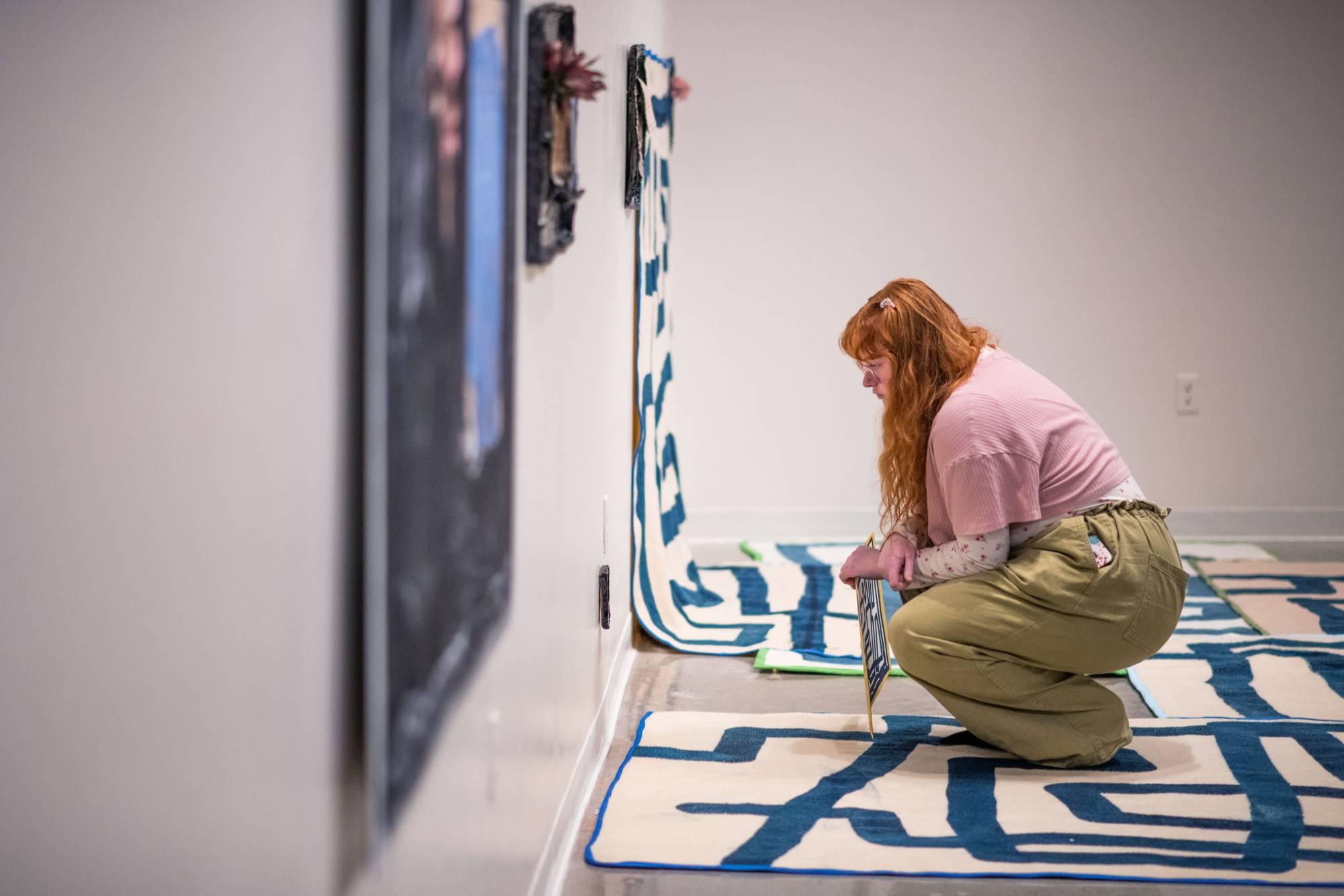 Visitor to the Padnos Gallery standing on an art installation by Emmy Bright, made up of wool rugs drawn on by a printmaking process to look like lines.